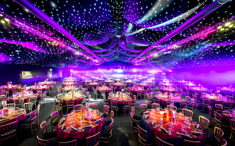 Lavish banquet hall setup with round tables, festive décor and sparkling star cloth ceiling at a shared Christmas party by Ultimate
